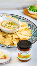 A decorative plate holds tortilla chips and creamy dip, while a jar of Terrapin Ridge Farms Mango Habanero Jam sits in front. A chip topped with the sweet and spicy jam is served on a small side plate.