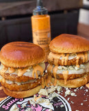 Two stacked chicken burgers with melted cheese, blue cheese crumbles, and Terrapin Ridge Farms Buffalo Ranch Squeeze on brioche buns sit on a wooden board. In the background is a bottle of Terrapin Ridge Farms Buffalo Ranch Squeeze.