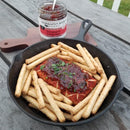 A cast iron skillet holds cheese topped with Terrapin Ridge Farms Hot Pepper Bacon Jam - 5 oz, a smoky bacon spread by Terrapin Ridge Farms, garnished with herbs and served with breadsticks on a rustic wooden table.