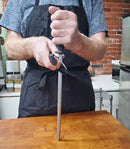 A man expertly holding SpitJack's Chef's Knife from the Barbecue Knife Bundle with Brisket Set, Sharpening Hone, Paring Knife, and Case, poised with precision.