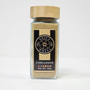 A 58g glass jar of Spice Wheel Coriander Powder, featuring a wooden lid, black label, and colorful dots at the bottom—ideal for enhancing your cooking with rich coriander flavor or adding a touch of cilantro to your favorite dishes.
