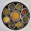 Introducing the Spice Wheel Italian Spice Wheel by Spice Wheel: a round metal spice box designed as a chic and practical spice organizer. This elegant set features nine small bowls, each filled with a unique Italian herb or spice, beautifully arranged in a circular pattern on a white background—making it the ideal kitchen gift for any culinary enthusiast.