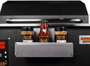 The Smokin Brothers Sauce & Rub Holder, a must-have grilling accessory from Smokin Brothers, is shown attached to a black grill or smoker. It conveniently displays three Smokin Brothers seasoning bottles—including two spice jars and one barbecue sauce bottle—on its sturdy metal shelf, keeping your favorite sauces and rubs easily accessible while you cook.