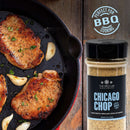 A skillet with grilled pork chops and garlic cloves sits next to a container from The Spice Lab Taste of America Seasoning Collection, showcasing the bold flavors of American-inspired blends that are ideal for BBQ cooking and grilling, all crafted by The Spice Lab.
