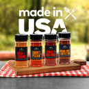 Four spice rub bottles from The Spice Lab Grilling Seasoning Collection—Bad to the Bone, Smoky Pecan, Sweet Rib Rub, and Ancho Chili + Coffee Rub—are arranged on a wooden board with a red plaid cloth. This gourmet gift set by The Spice Lab highlights premium BBQ seasoning blends in every bottle. Text above reads made in USA.