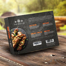 Outdoors on a wooden table sits a box labeled The Spice Lab Grilling Seasoning Collection, featuring grilled meat skewers and descriptions of four premium BBQ seasoning blends—Bad to the Bone, Sweet Rib Rub, Ancho Chili + Coffee Rub, and Smoky Pecan—making it an ideal grilling gift set for barbecue enthusiasts from The Spice Lab.