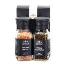 Two glass grinders—one with pure Himalayan Pink Salt and the other with premium black peppercorns—are displayed side by side in front of a sleek black and white box, creating The Spice Lab Himalayan Pink Salt & Premium Black Pepper Grinder Set by The Spice Lab.