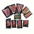 A selection of raw steaks from the Dude Food High Steaks Box—including premium Kansas City Strip Steaks, Skirt Steaks, and T-Bones by Dude Food—are individually vacuum sealed in black plastic and arranged on a white background with a Dude Food card at the center.