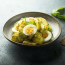 A bowl of potato salad mixed with green pesto and delicate fines herbs, topped with sliced hard-boiled eggs and garnished with The Spice Lab Fancy Chervil by The Spice Lab, arranged on a dark textured surface.
