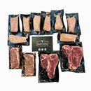 The Dude Food Guys Meat Box by Dude Food features vacuum-sealed assorted raw meat cuts, such as boneless chicken breasts and Kansas City Strip Steaks, presented around a black card marked with five stars—all beautifully displayed on a white background—making it the perfect essential for your ultimate game day snacks.