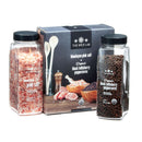 Two clear containers—one with coarse Himalayan pink salt and the other filled with organic black Tellicherry peppercorns—stand beside a box labeled The Spice Lab Himalayan Pink Salt Coarse & Organic Black Tellicherry Peppercorns Combo Pack from The Spice Lab. The packaging is adorned with images of salt, pepper, and wooden utensils, emphasizing this premium spice duo.