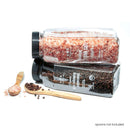 Two clear jars from The Spice Lab, one filled with coarse Himalayan pink salt and the other with whole organic black Tellicherry peppercorns, are stacked. Wooden spoons holding salt and pepper sit beside them. Text reads: Spoons not included. The set is labeled as The Spice Lab Himalayan Pink Salt Coarse & Organic Black Tellicherry Peppercorns Combo Pack.