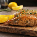 Grilled chicken breast garnished with herbs on a wooden board, enhanced with a touch of The Spice Lab Seafood Seasoning Collection by The Spice Lab, and served with lemon wedges on the side.