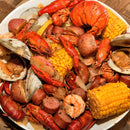 A plate piled high with lobster, crawfish, shrimp, clams, corn on the cob, potatoes, and slices of sausage—all expertly seasoned and blended together using The Spice Lab Seafood Seasoning Collection by The Spice Lab.