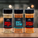 Three spice bottles from The Spice Lab Best Seller Seasoning Set—Smoked Butchers Blend, Spicy Seafood, and Nashville Hot Chicken seasoning—are displayed on a wooden surface with a blurred background. This premium set from The Spice Lab is perfect for adding bold flavor to your favorite dishes and is an excellent addition to any grilling spice collection.