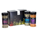 Three spice jars labeled Herbs de Provence, French Onion + Garlic, and Rosemary Roasted Garlic are arranged in front of a sleek black box adorned with vibrant spice illustrations—offering an enticing first look at The Spice Lab Flavors of Provence Seasoning Set. Created by The Spice Lab, these gourmet blends are perfect for French and Italian-inspired recipes, bringing authentic flavor to elevate any meal.