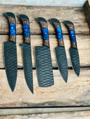 The Texan Knives Handmade Damascus Steel Chef Knife Set features five knives with unique wood and blue resin handles—beautifully arranged on a rustic wooden surface—making it an ideal Valentine’s Day or wedding gift for culinary enthusiasts.