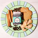A green and blue plate displays gingerbread cookies, fresh ginger, cinnamon sticks, whole cloves, allspice, and a small tin of Spicewalla Gingerbread Spice by Spicewalla—an ideal way to add the cozy warmth of traditional gingerbread flavors to your holiday baking.