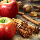 Two red apples rest on a rustic wooden surface beside a bundle of The Spice Lab Organic Cinnamon Sticks tied with twine, surrounded by star anise, walnuts, and loose cinnamon sticks—perfectly capturing the cozy essence of mulled wine season.