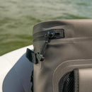 Close-up of the Bob The Cooler Co. 25L "The Bro" Backpack Soft Cooler in gray, featuring a waterproof design with a zipper and pull tab, resting on a boat with blurred greenish water in the background.