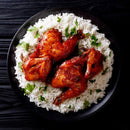 A black plate with roasted chicken pieces, seasoned with The Spice Lab Organic Ground Ginger, served on a bed of white rice and garnished with chopped fresh herbs, displayed on a dark wooden surface.