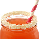 A close-up of an orange drink in a glass jar with a white and pink striped straw, featuring a rim coated in The Spice Lab Key Lime Salt Cocktail Rimmer by The Spice Lab—providing the perfect finishing touch for any margarita or cocktail creation.
