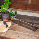 A WPPO LLC Direct Wood-Fired Oven Flame / Heat Deflector sits on a wooden counter beside potted plants, a cutting board dusted with flour, and a knife—an essential accessory for chefs who value quality pizza oven tools in their wood-fired ovens.