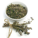 A white bowl filled with dried herbs, featuring The Spice Lab Organic Whole Thyme—an excellent choice for French, Italian, and Mediterranean cooking—sits next to a small bundle of dried flowering herbs tied with twine, all against a white background.