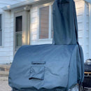 A WPPO Karma Series Wood-Fired Oven, protected by a WPPO LLC Direct premium oven cover, stands on a patio in front of a white house with windows and a door.