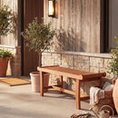 The 2-Person Outdoor Wood Bench with Slatted Seat - Set of 2 by DirectDeals is placed on a stone porch near potted plants and a basket with a blanket, creating cozy patio seating in sunny weather.
