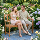 A smiling couple relaxes on the DirectDeals 2-Person Acacia Wood Garden Bench with X-Shaped Backrest in a vibrant flower garden, with a small table and teacup nearby under the sunny sky.
