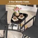 The DirectDeals 2-Seater Outdoor Glider Bench with Center Table holds flowers, iced coffee, and pastries above, with books and a chess set below for a cozy outdoor setup. Two black patio chairs sit on either side.