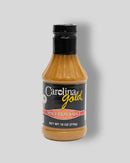 An 18-ounce bottle of Gourmet Carolina Gold Spicy Hot Sauce, a mustard-based barbecue sauce featuring a black cap and a bold, gourmet flavor profile.