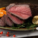 Slices of medium-rare roast beef on a plate, seasoned with The Spice Lab Special Extra Bold Indian Black Peppercorns and garnished with rosemary, orange slices, and bread, all set atop a festive tablecloth.