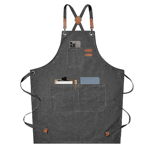 A dark gray apron with brown leather accents featuring three front pockets, one holding a phone, another holding a clipboard and pen, and the third holding a closed notebook.