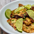 Grilled fish fillets garnished with fresh lime wedges and a sprinkle of The Spice Lab Whole Leaf Cilantro by The Spice Lab, served on a white plate on a wooden table.