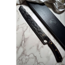 The Spaceman Knives Meteor Series Brisket Slicer features a hammered blade and wooden handle, shown on marble beside its black presentation box—ideal for BBQ carving or slicing smoked meats.