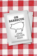 A packet featuring a pig illustration and the text "On Barbecue - Paperback" from Books by splitShops rests on a red and white checkered tablecloth, perfectly capturing the spirit of North Carolina barbecue and its rich history.