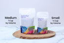 Two standing pouches of World Spice Hibiscus from World Spice, labeled Medium (1 cup by volume) and Small (½ cup by volume), are placed on a wooden board against a marble background—ideal for those looking to craft vibrant hibiscus cocktails or enjoy a soothing cup of tea made from the finest hibiscus flowers.