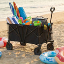 A DirectDeals 38 Inch 400 LBS Heavy-Duty Collapsible Wagon Cart with Adjustable Handle for Camping Garden-Black holds towels, toys, and a cooler on the beach near inflatable swim rings, with the ocean behind.