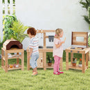Two kids play with the DirectDeals 3-Piece Outdoor Kitchen Set Mud Kitchen with Separate BBQ Grill and Pizza Oven-Natural in a grassy yard, surrounded by plants, toy food, and utensils. One checks the oven while another enjoys a popsicle.
