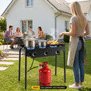 A woman uses the 3 Burner Propane Stove 240000 BTU Outdoor Camping Grill by DirectDeals outdoors while four people sit nearby. Red gas cylinder shown is not included.
