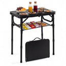 A DirectDeals 3-Height Folding Camping Table with Large Storage Net & Handle holds snacks, fruit, and drinks on top, has packaged snacks below, and a closed portable case leaning against one leg.