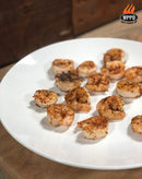 A white plate filled with several cooked, seasoned shrimp rests on a wooden surface, perfectly evoking the rustic charm of outdoor cooking. The shrimp are casually arranged, suggesting they were freshly grilled in a WPPO Le Peppe Portable Wood-Fired Pizza Oven by WPPO LLC Direct. The WPPO Get Fired Up logo is displayed in the top right corner.