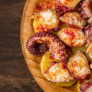 Sliced octopus and potatoes sprinkled with The Spice Lab Organic Smoked Paprika for a smoky-sweet flavor, served on a wooden plate atop a dark wooden surface.