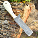 The Texan Knives Gareth Bull Style Knife features an 8" Damascus steel blade and a light camel bone handle, displayed outdoors on a tree log. Includes a Western leather sheath.