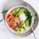 A bowl with smoked salmon, cucumber ribbons, arugula, and a poached egg, garnished with pepper and a sprinkle of The Spice Lab Hawaiian Red Alaea Sea Salt Fine Grain. The bowl sits on a gray plate with a fork and some arugula leaves.