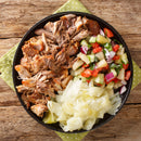 A plate featuring shredded roasted pork seasoned with The Spice Lab Hawaiian Red Alaea Sea Salt Fine Grain, accompanied by a chopped cucumber salad with tomatoes and onions and steamed cabbage, served on a green polka dot napkin atop a rustic wooden table.