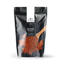 A black resealable bag labeled The Spice Lab Hawaiian Red Alaea Sea Salt Medium Grain, from The Spice Lab, features an image of coarse red salt and a wooden spoon on the front. Known for its earthy flavor, this sea salt has a net weight of 2 lbs.