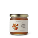 A glass jar of Georgetown Olive Oil Co. Raw Unfiltered Varietal Honey with a gold lid and a white label featuring an illustration of orange blossoms, labeled with a net weight of 9.5 oz (269 g). This raw and unfiltered honey beautifully captures the delicate essence of blooming orange blossoms.